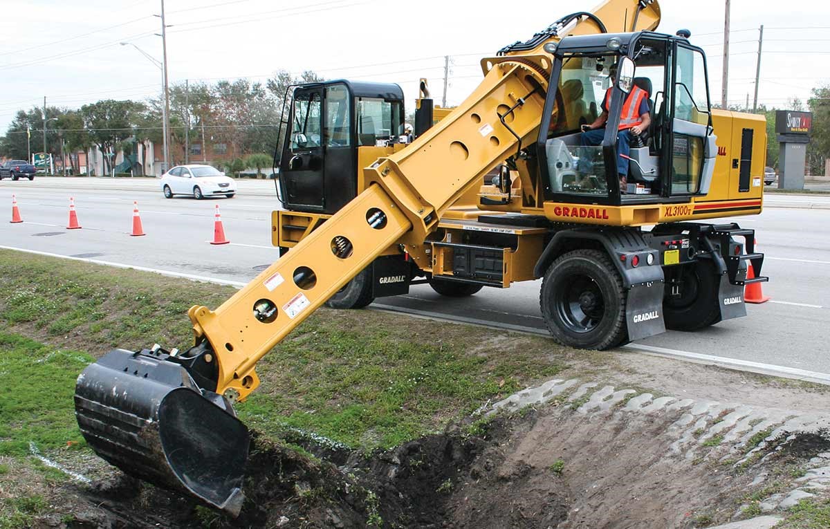 A Gradall Highway Speed Wheeled Excavator digs at the side of a road.