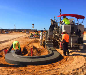 Workers forming a curb using a curb machine.